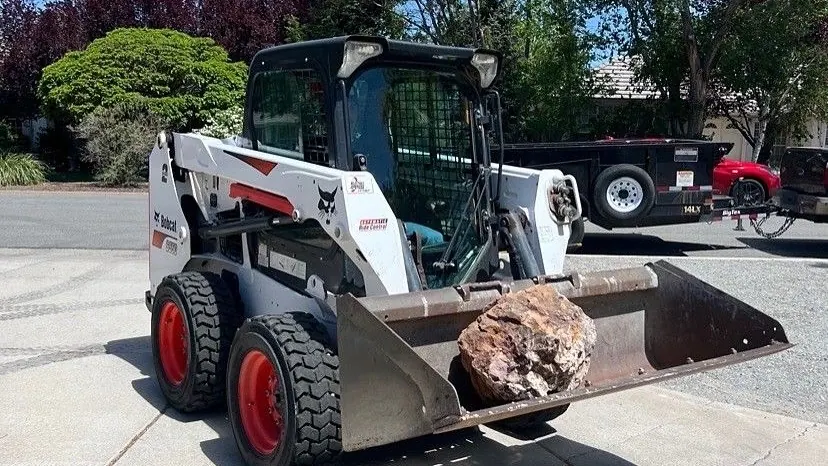 A skid steer carrying a boulder in its bucket