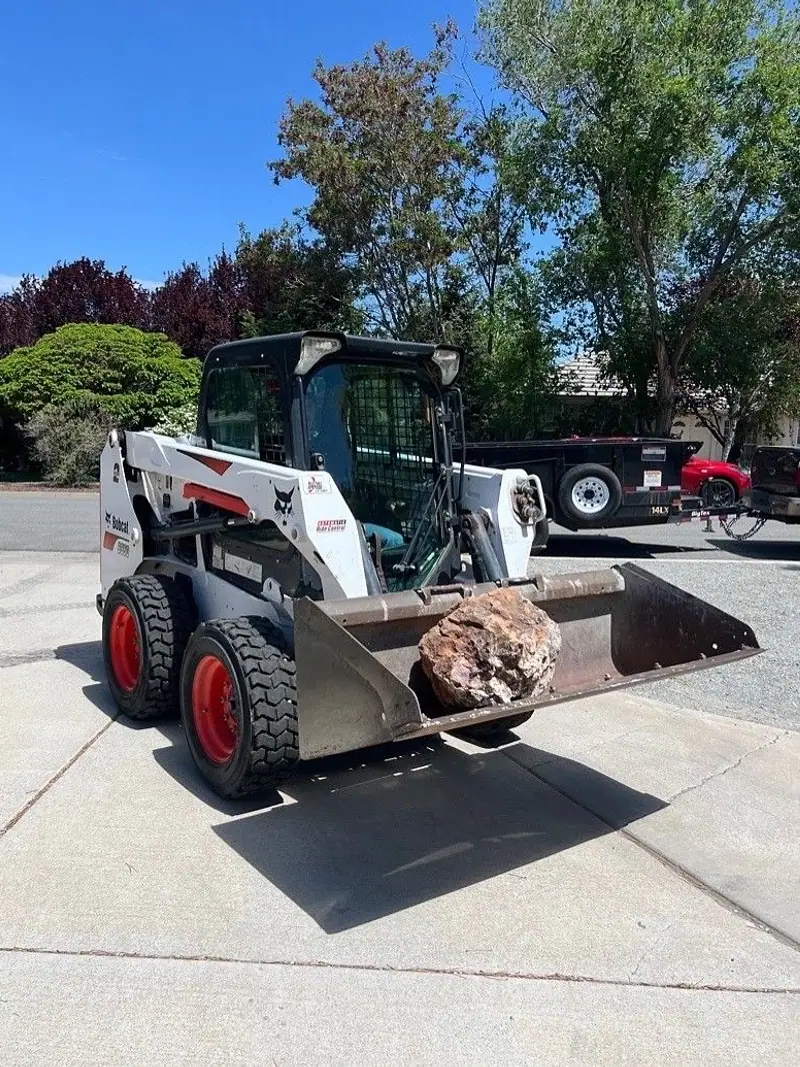 A skid steer carrying a boulder in its bucket