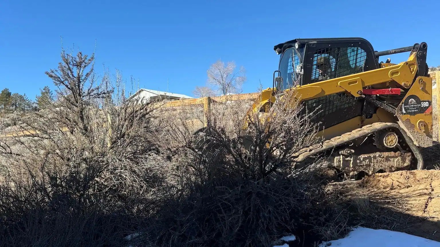 A skid steer clearing sagebrush on a snowy lot
