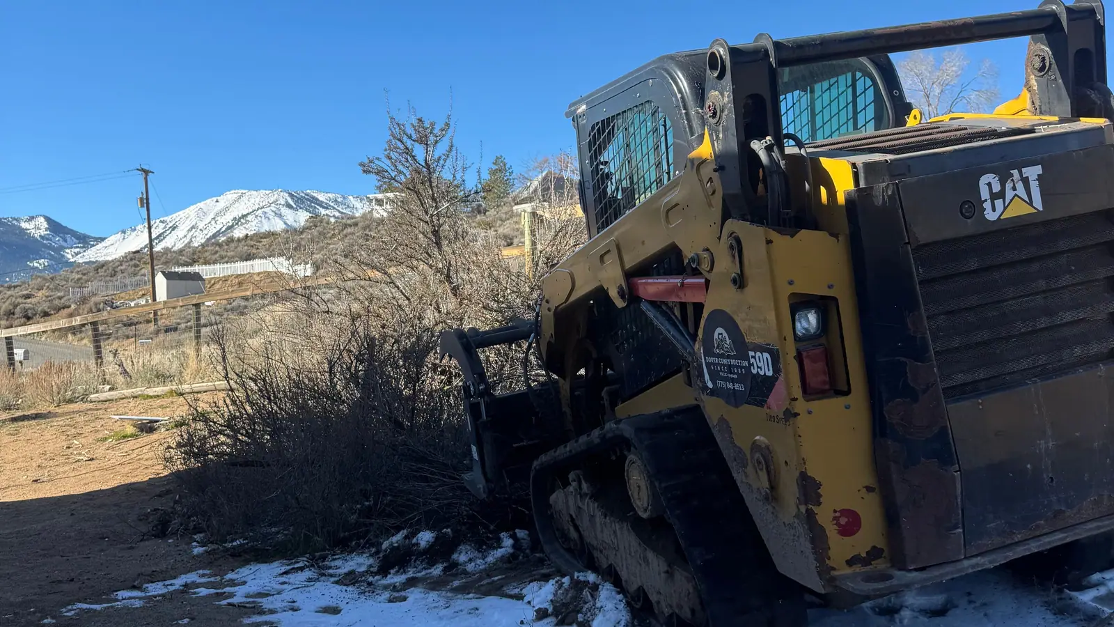 A skid steer clearing brush on a snowy lot