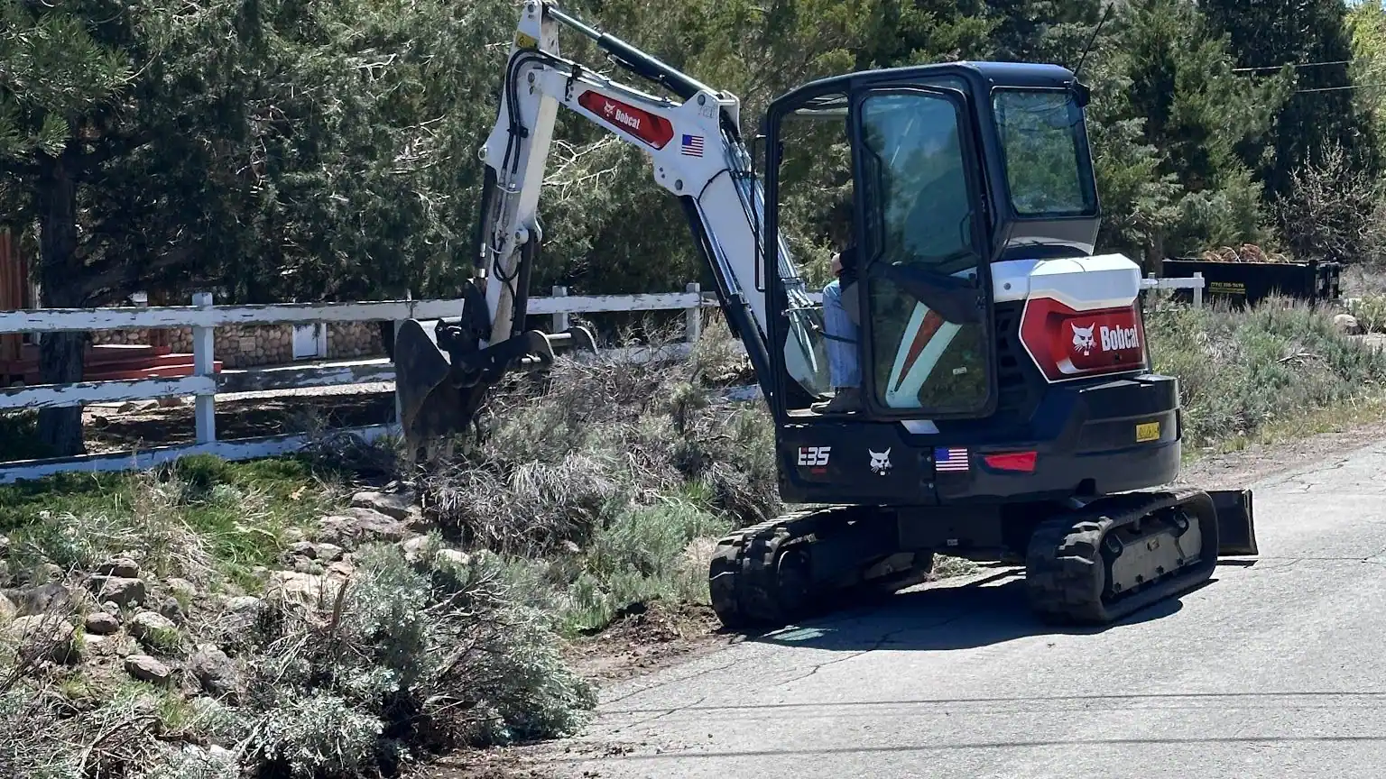 A mini excavator at work along a fence line