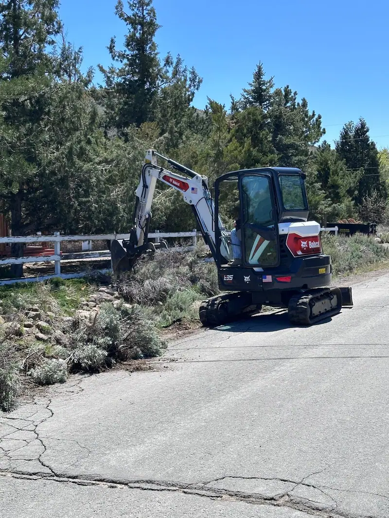 A mini excavator at work along a fence line