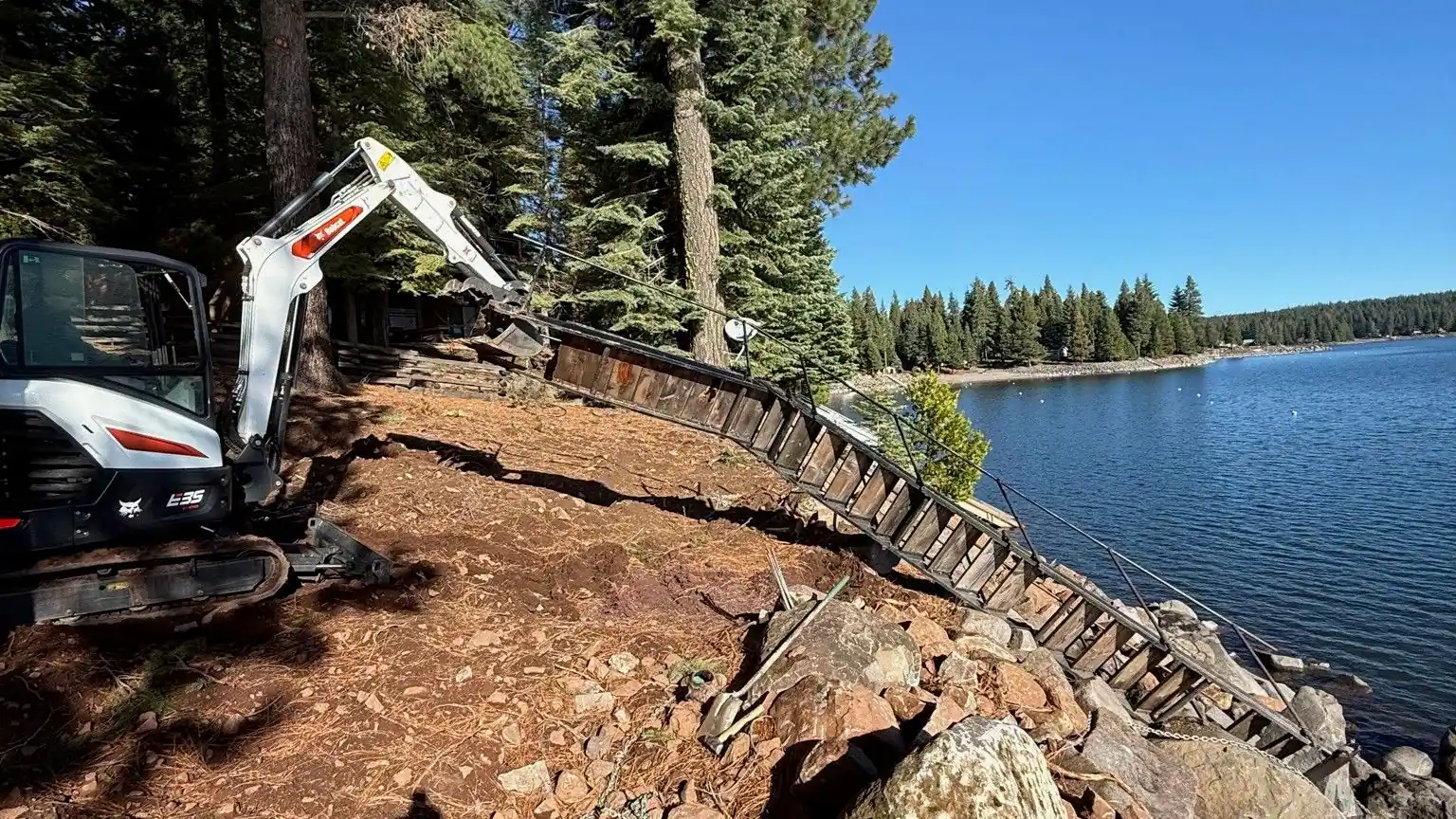 A mini excavator working rock along a lake shoreline