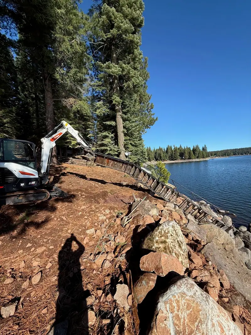 A mini excavator working rock along a lake shoreline