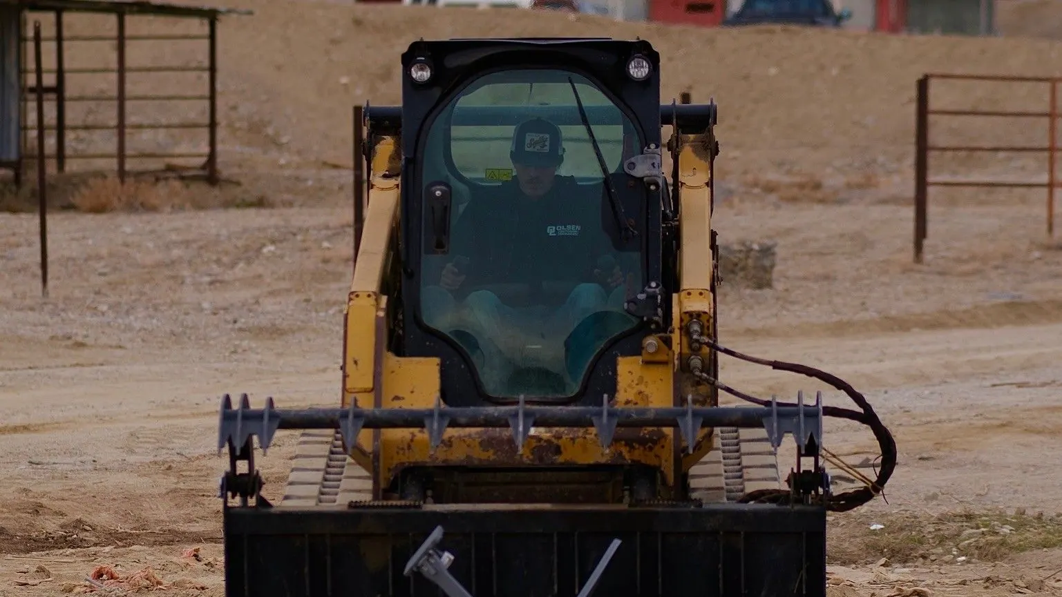 A skid steer with a grapple in front of broken lumber on a dirt lot