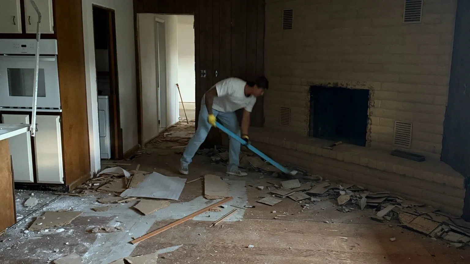 A worker scraping old flooring off a living room floor