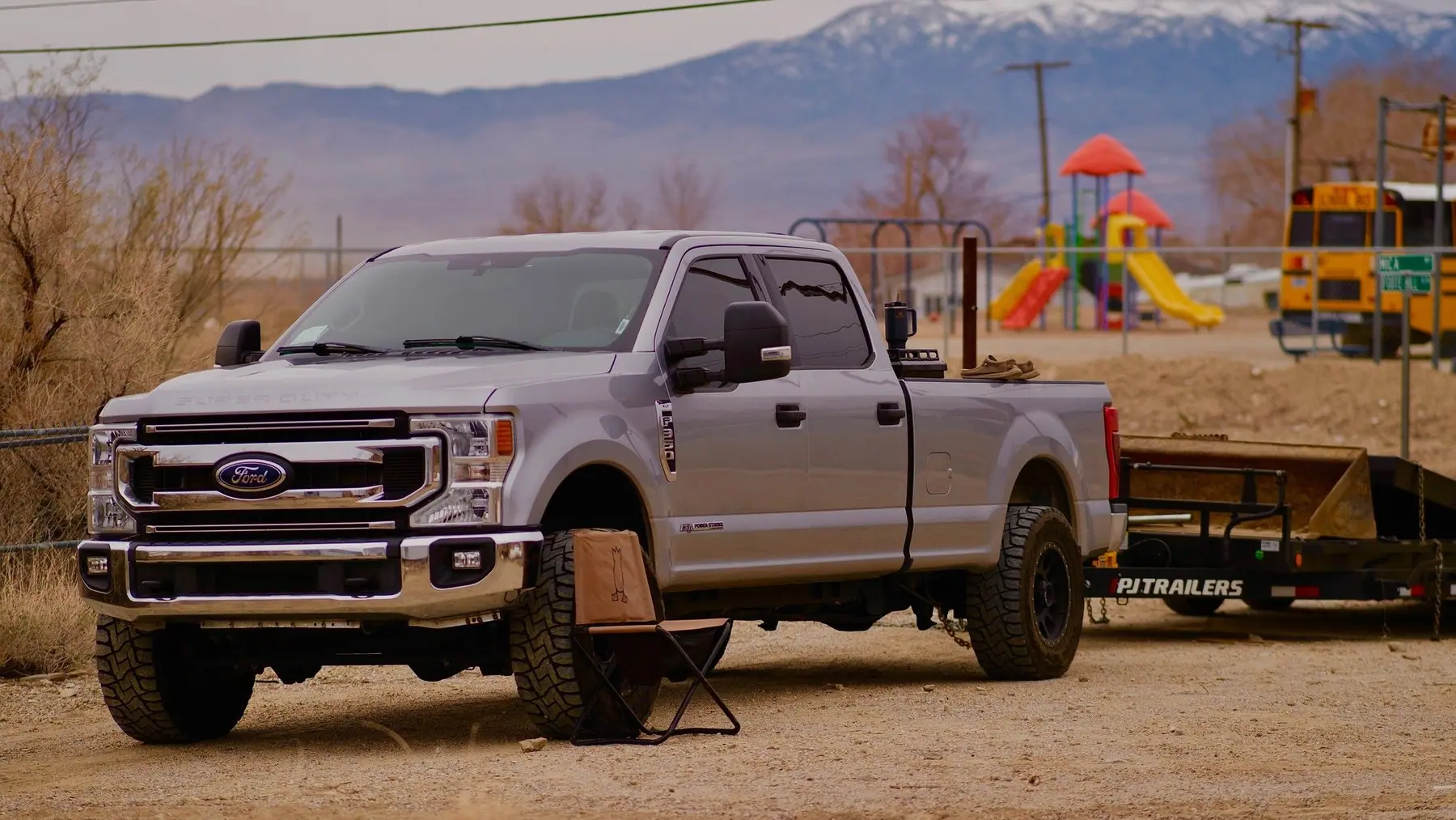The silver Ford pickup with its trailer parked on a dirt lot with snowy mountains behind