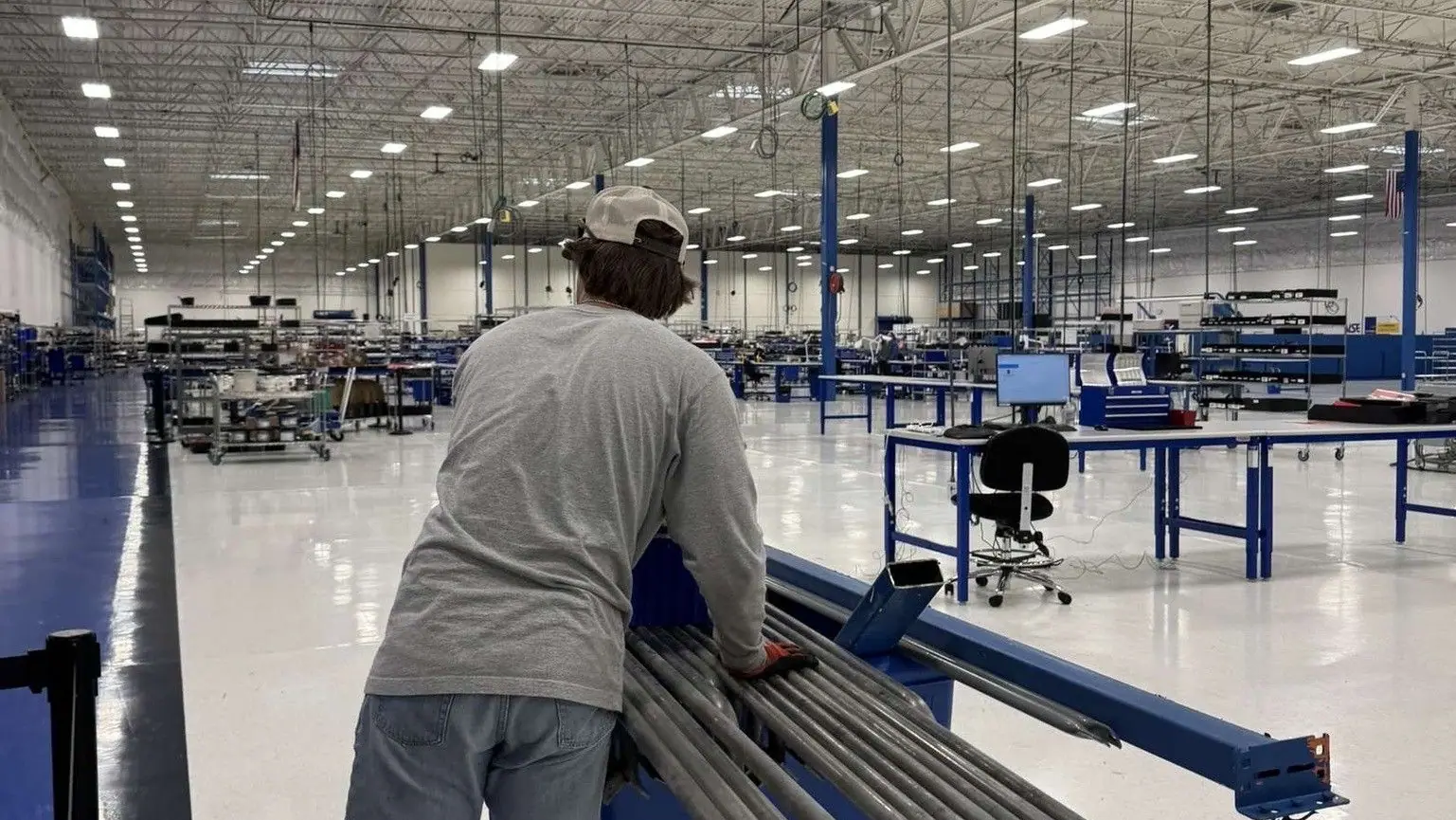 A worker pushing a cart of metal parts across a warehouse floor