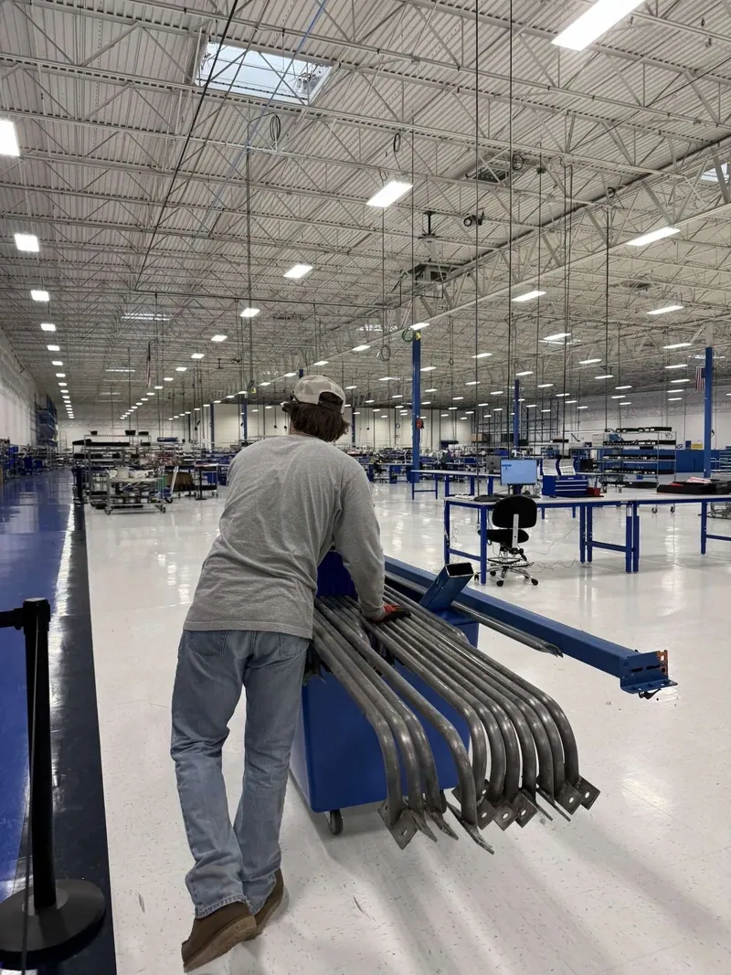 A worker pushing a cart of metal parts across a warehouse floor