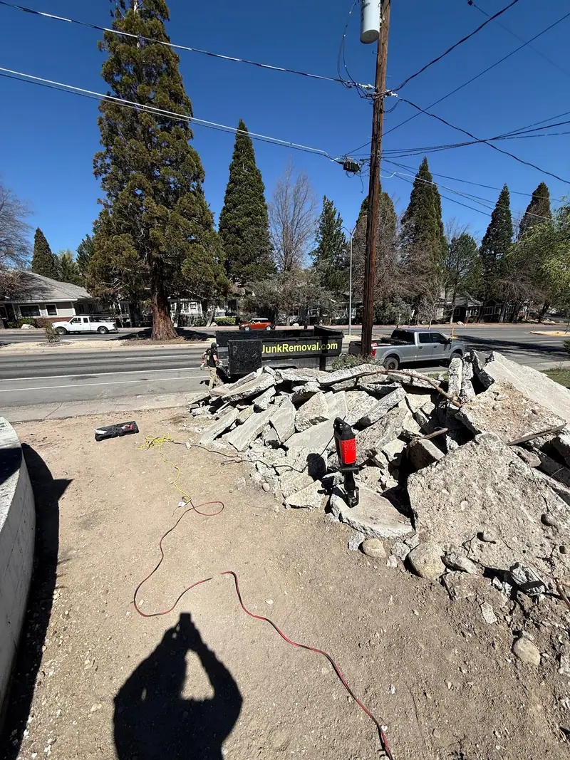 Broken concrete slabs piled by the curb next to a roll-off dumpster