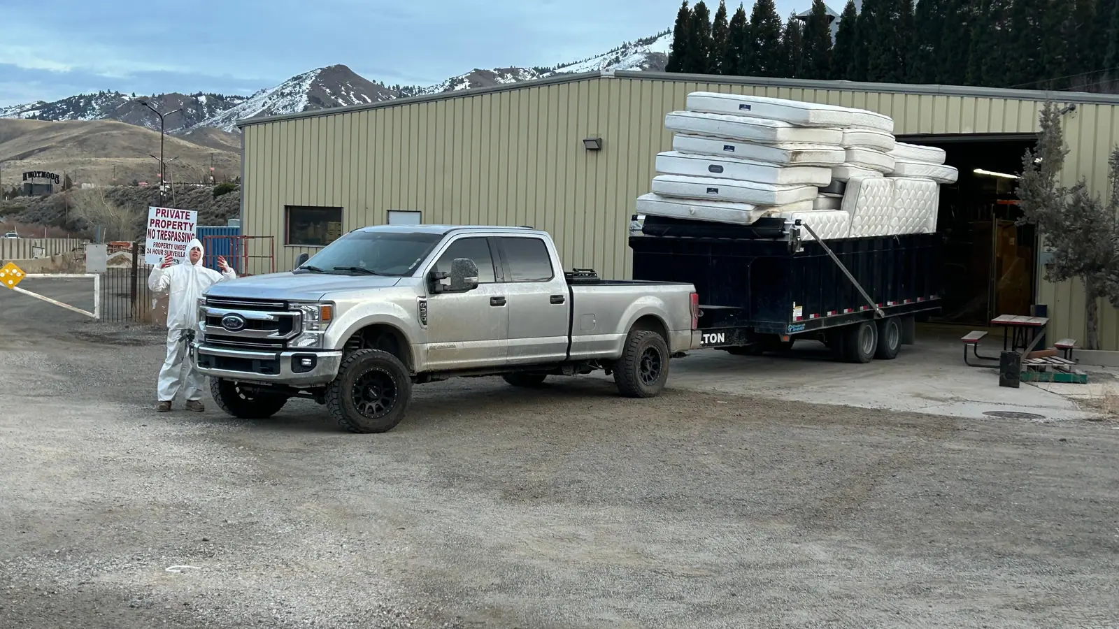 The silver pickup and black dump trailer stacked high with mattresses at a warehouse