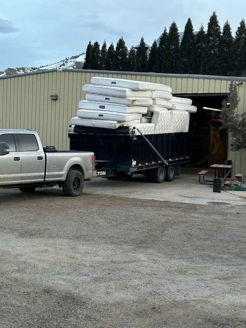 The silver pickup and black dump trailer stacked high with mattresses at a warehouse
