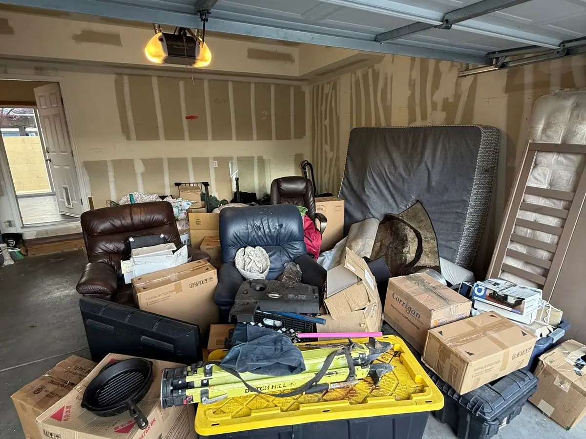 A garage packed with recliners boxes bins and a mattress