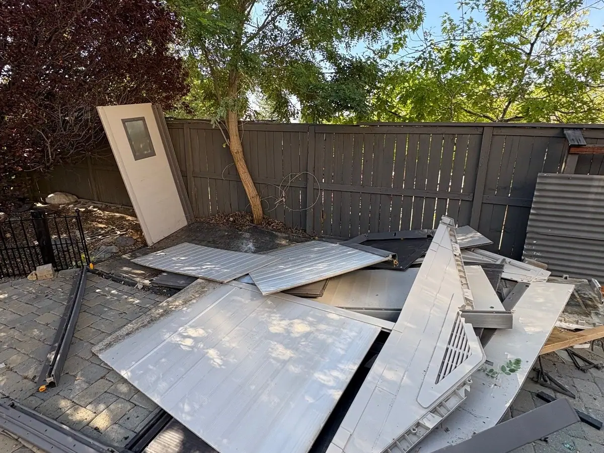 Metal shed panels and a frame piled on a paver patio by a fence