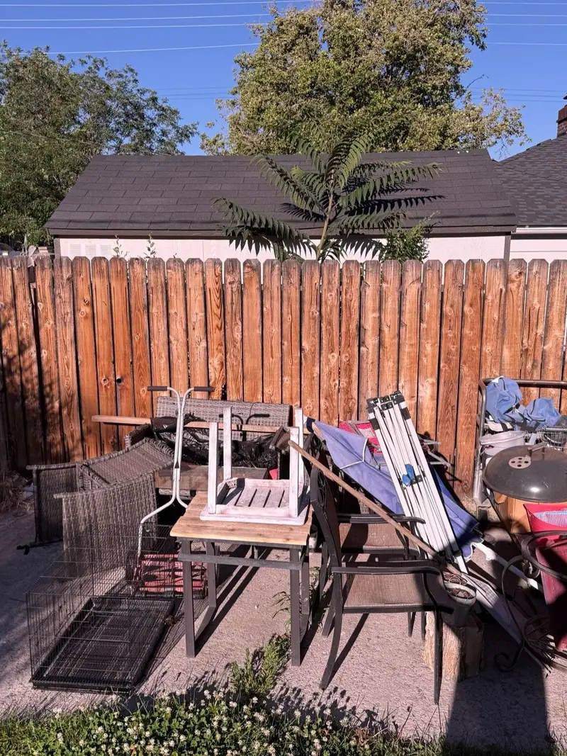 Old chairs a grill and scrap piled in a fenced backyard