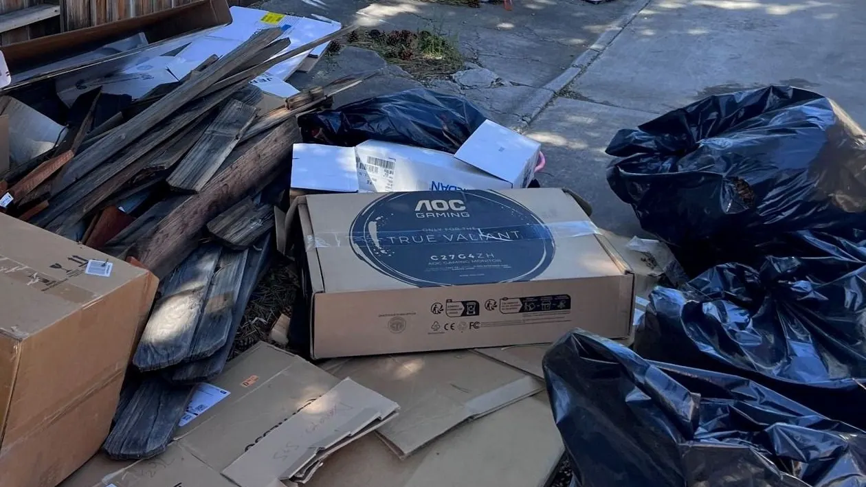 A computer monitor box and other boxes piled with trash bags at a side yard