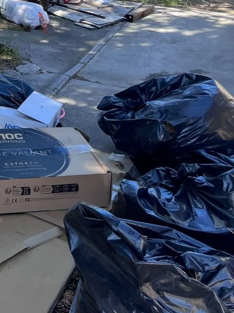 A computer monitor box and other boxes piled with trash bags at a side yard