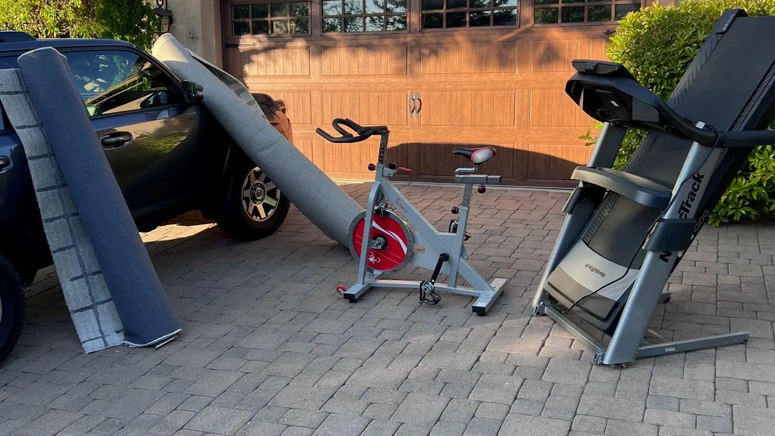 A treadmill exercise bike and old shelving set out on a paver driveway