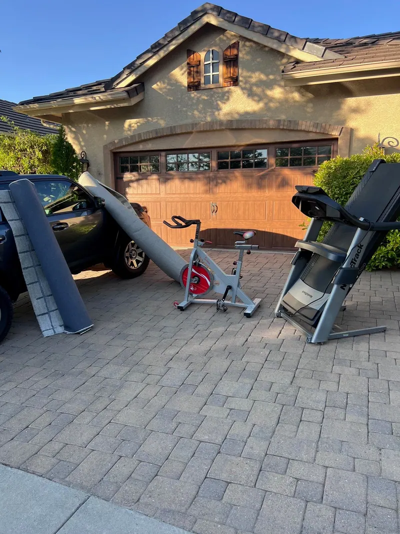 A treadmill exercise bike and old shelving set out on a paver driveway