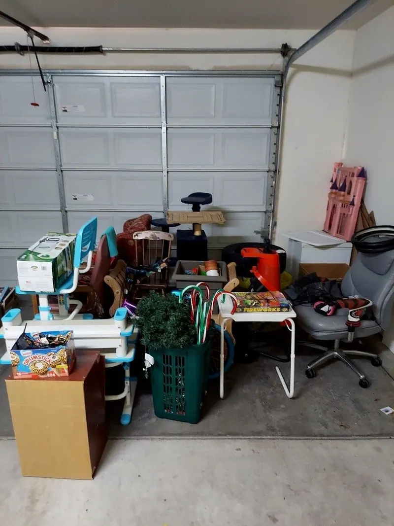 A garage crowded with chairs bins and boxes