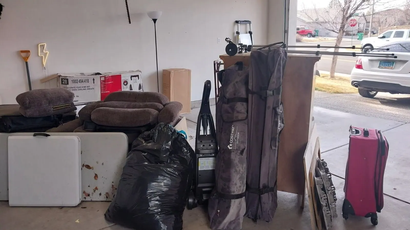 A loveseat bags tables and luggage lined up in an open garage