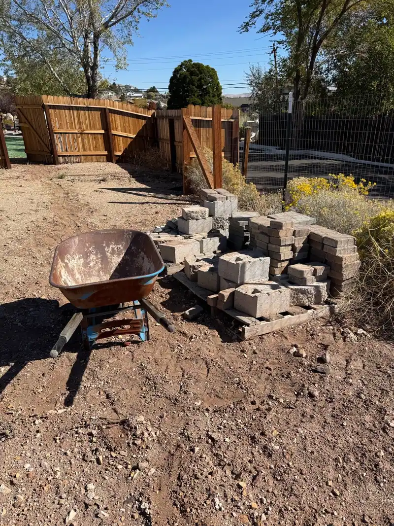 Old pavers and a wheelbarrow piled in a backyard