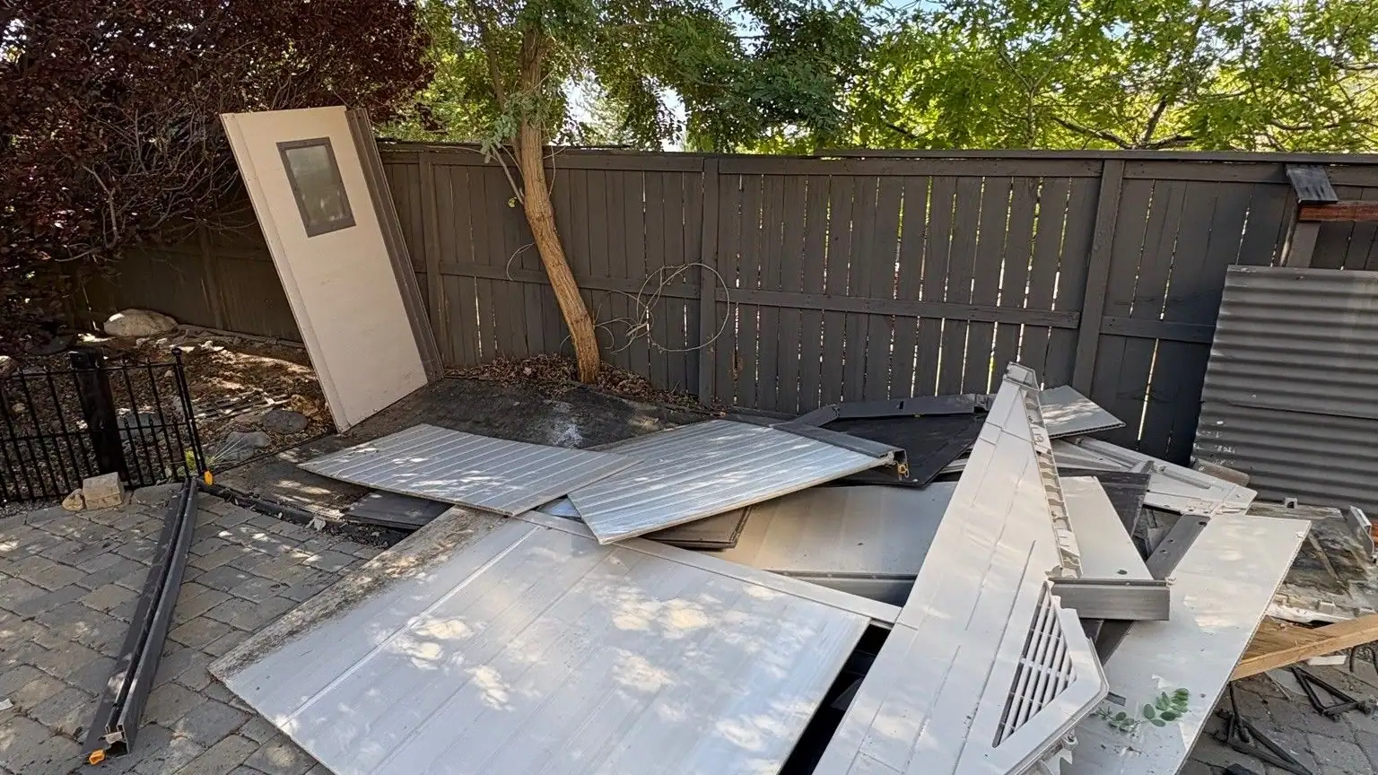 Metal shed panels and a frame piled on a paver patio by a fence