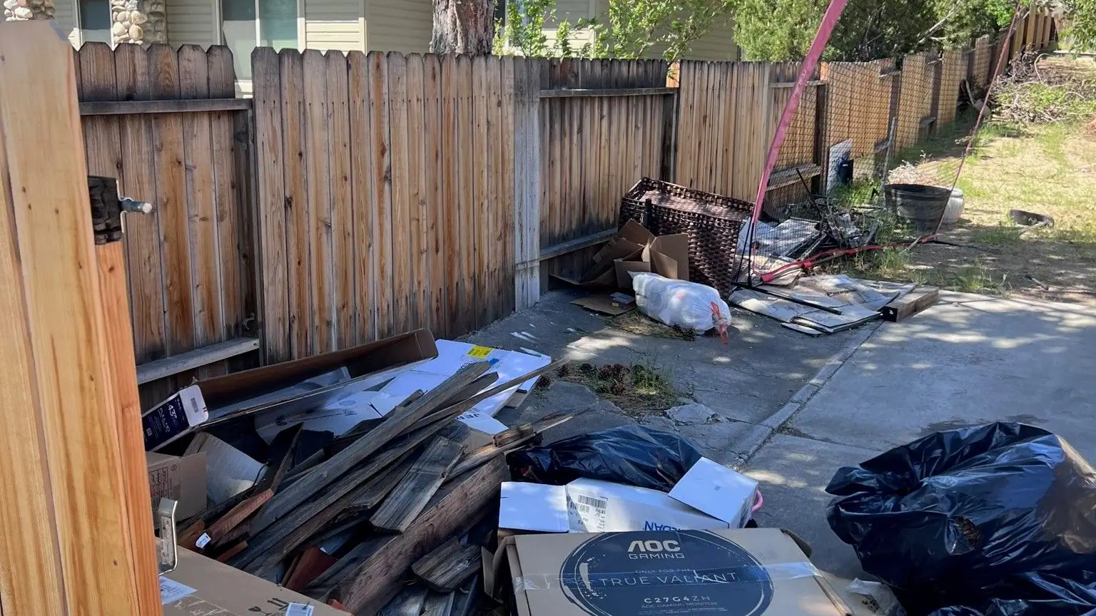 Boxes bags and scrap wood piled along a side yard fence