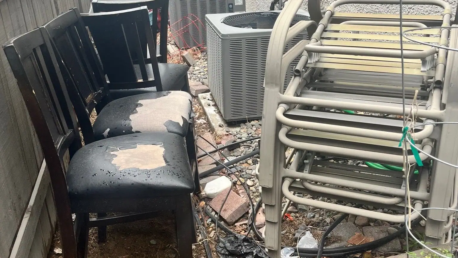 Old chairs and patio furniture stacked in a narrow side yard