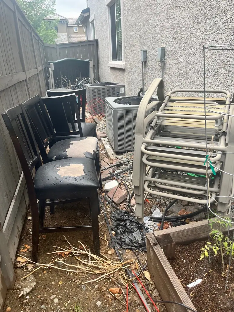 Old chairs and patio furniture stacked in a narrow side yard