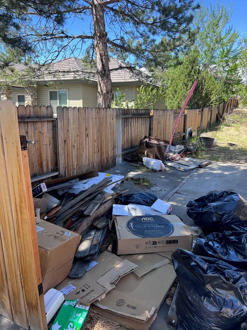 Boxes bags and scrap wood piled along a side yard fence