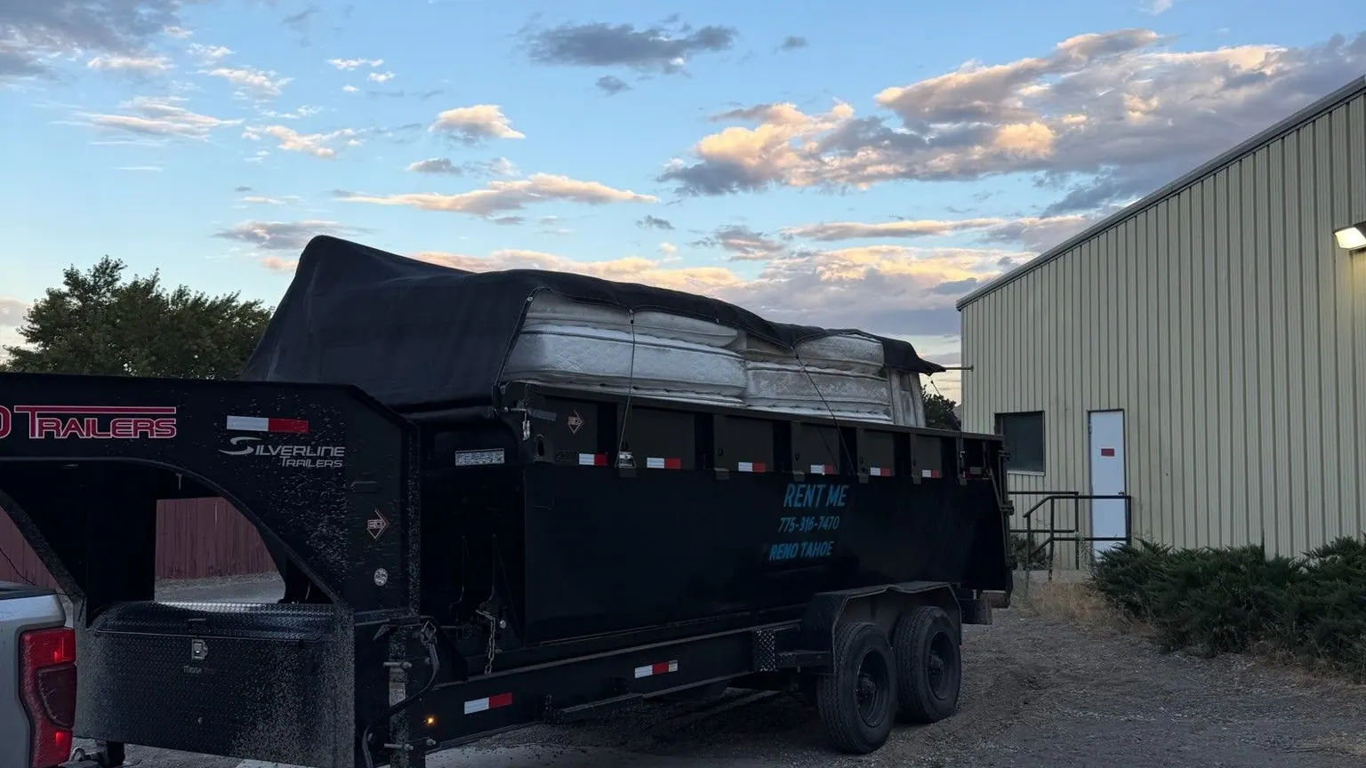 The black dump trailer tarped over a full load beside a commercial building