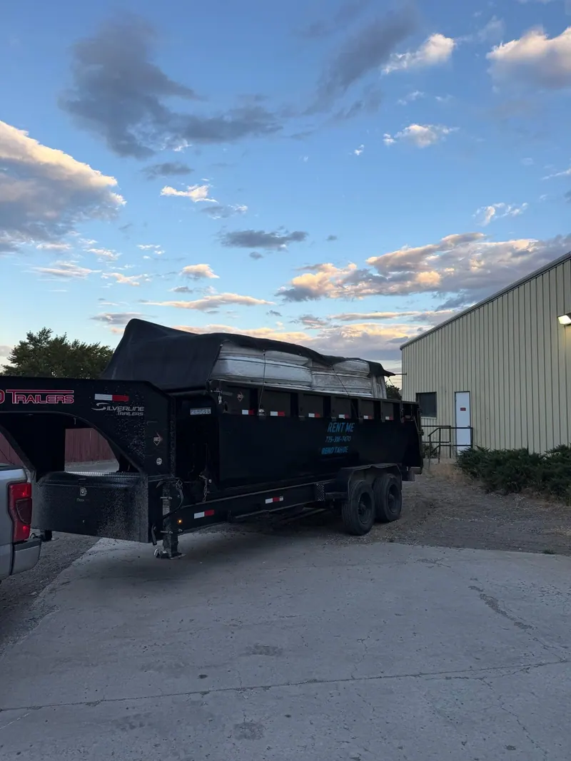 The black dump trailer tarped over a full load beside a commercial building