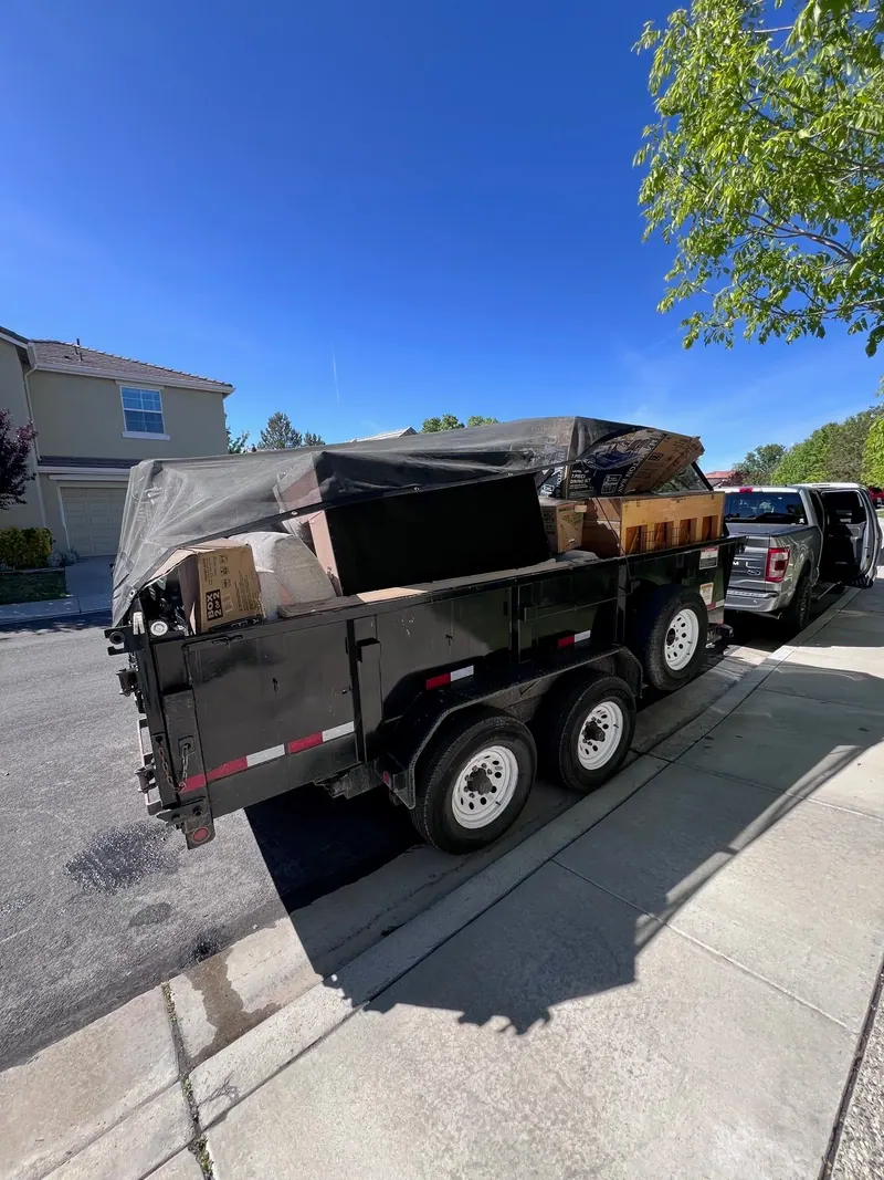 The black dump trailer loaded and tarped at the curb with the pickup ahead of it