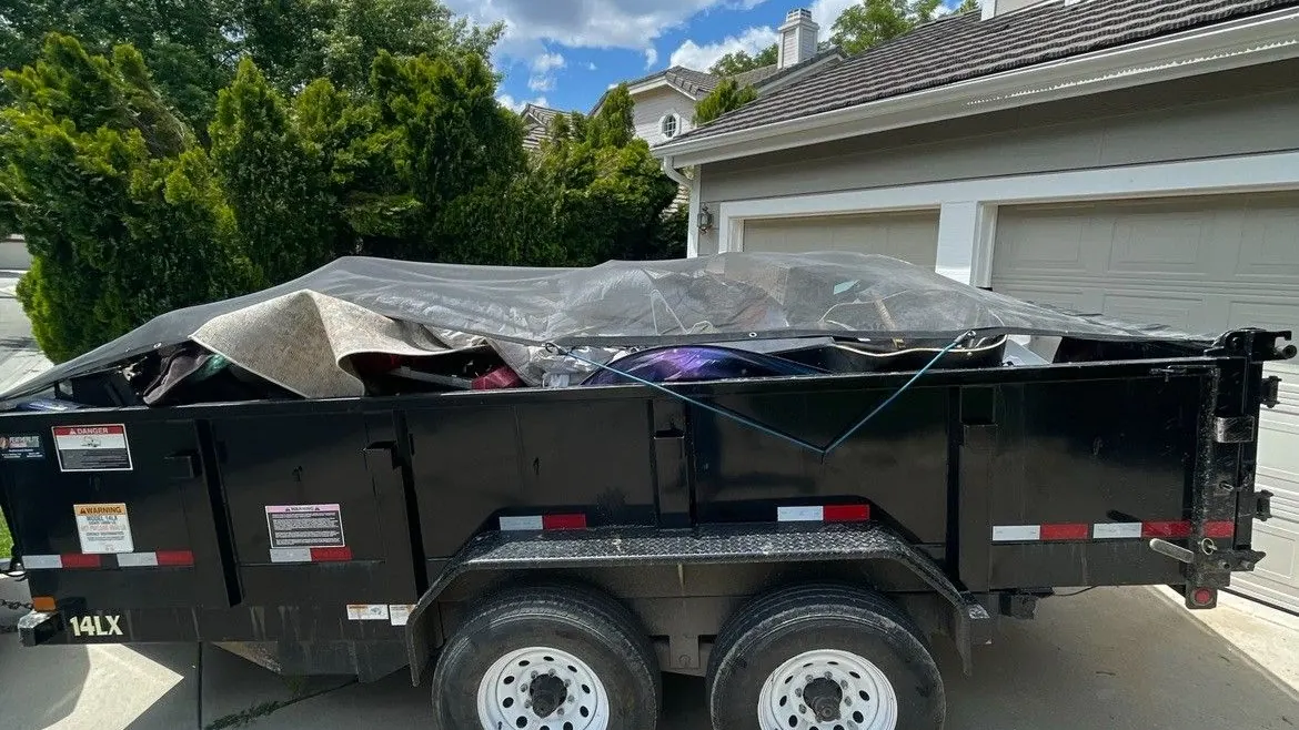 The black dump trailer loaded and tarped in a driveway