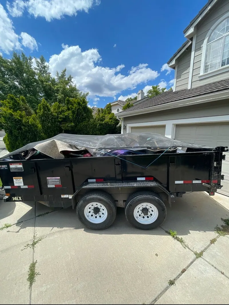The black dump trailer loaded and tarped in a driveway