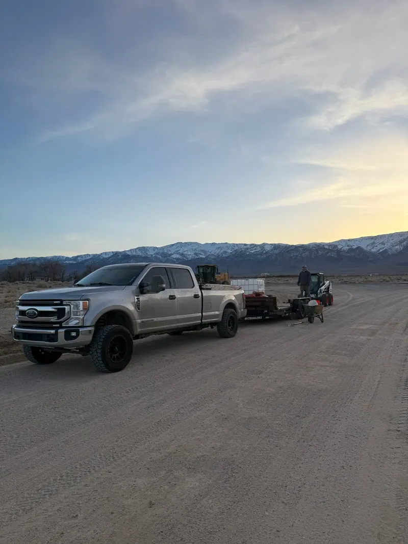 The silver pickup and trailer on an open road at dusk with mountains behind