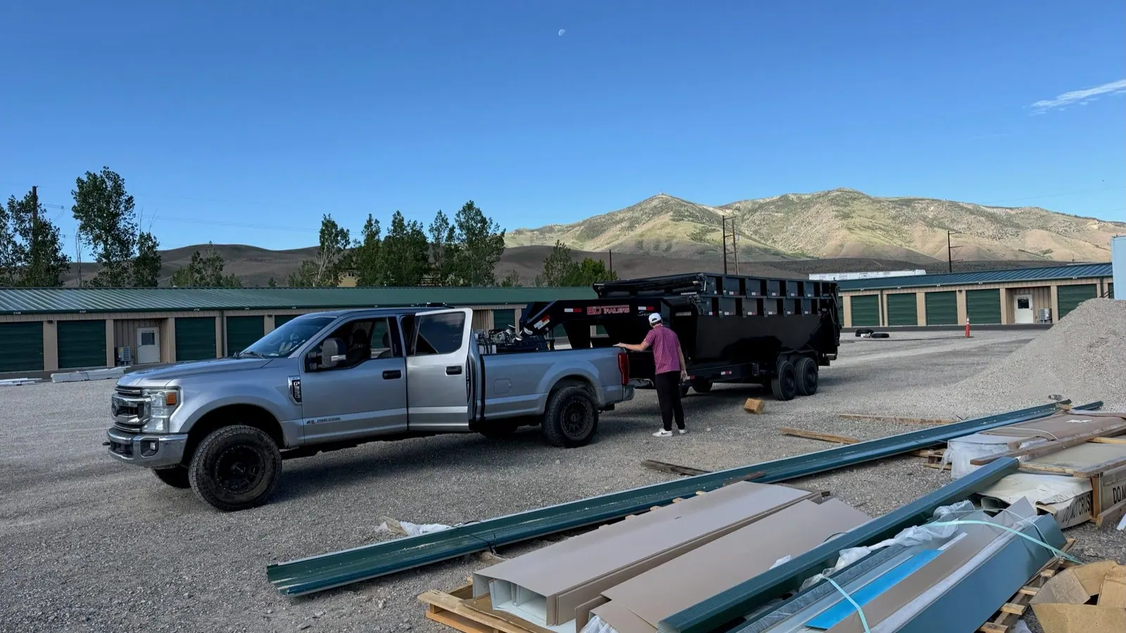 The pickup and dump trailer at a storage lot beside a stack of building materials