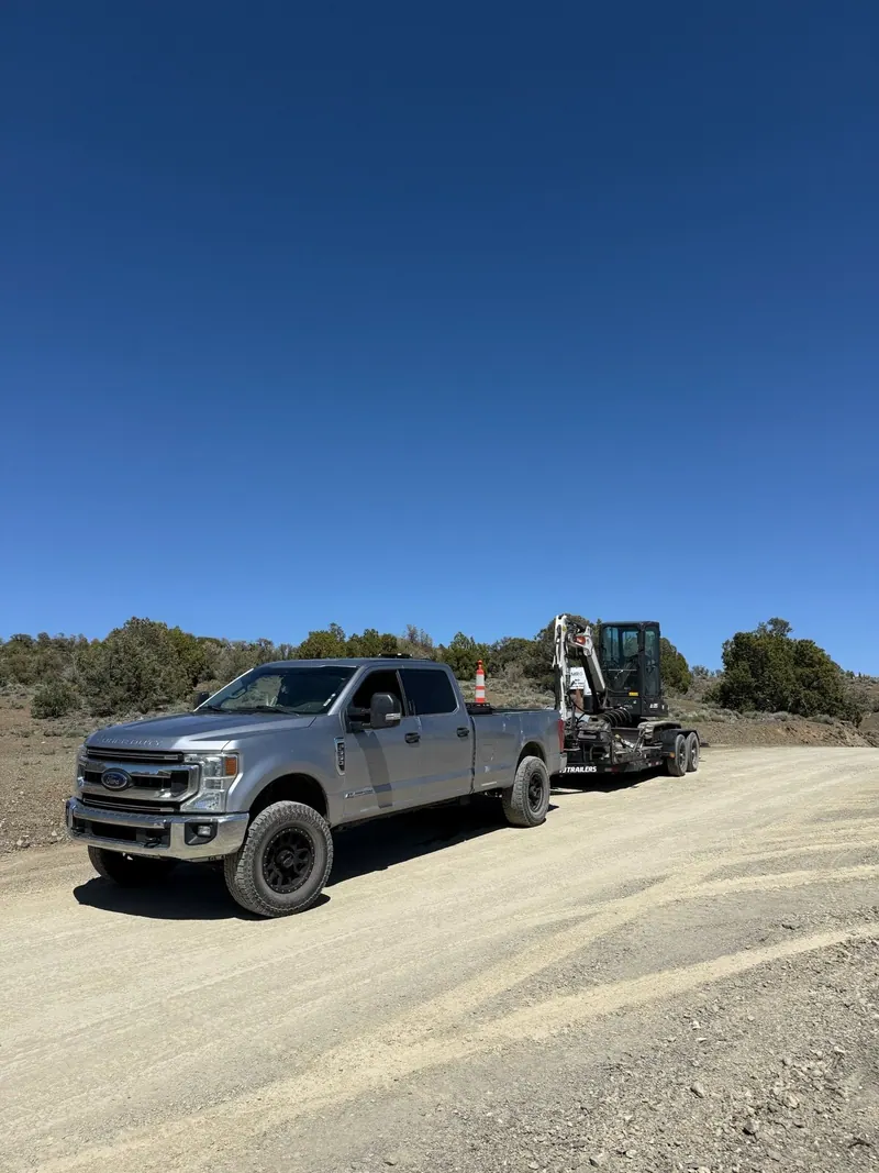 The silver pickup towing a trailer down a dirt road